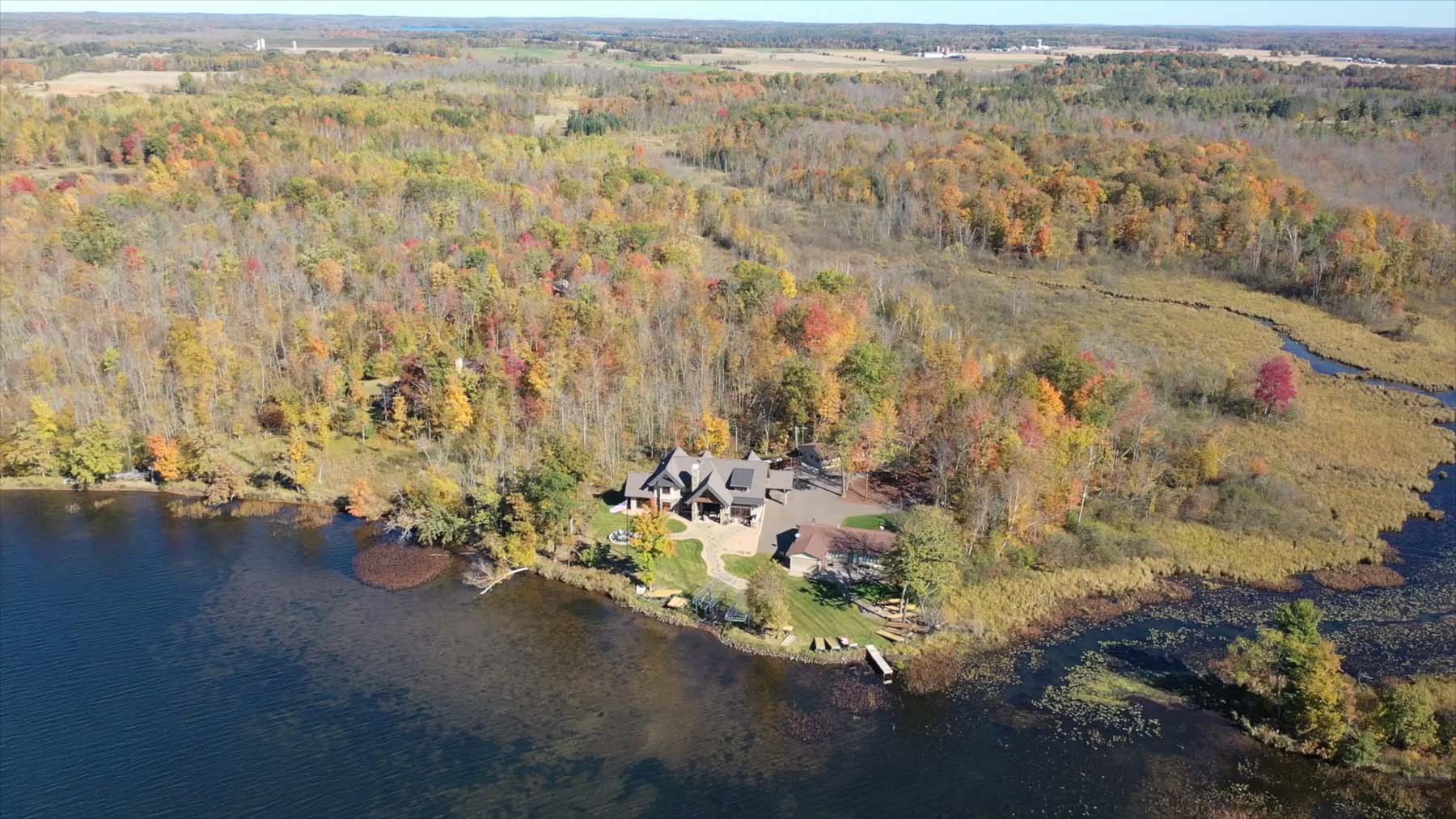 Aerial view of a Balsam Lake cabin surrounded by dense autumn foliage and a winding shoreline.